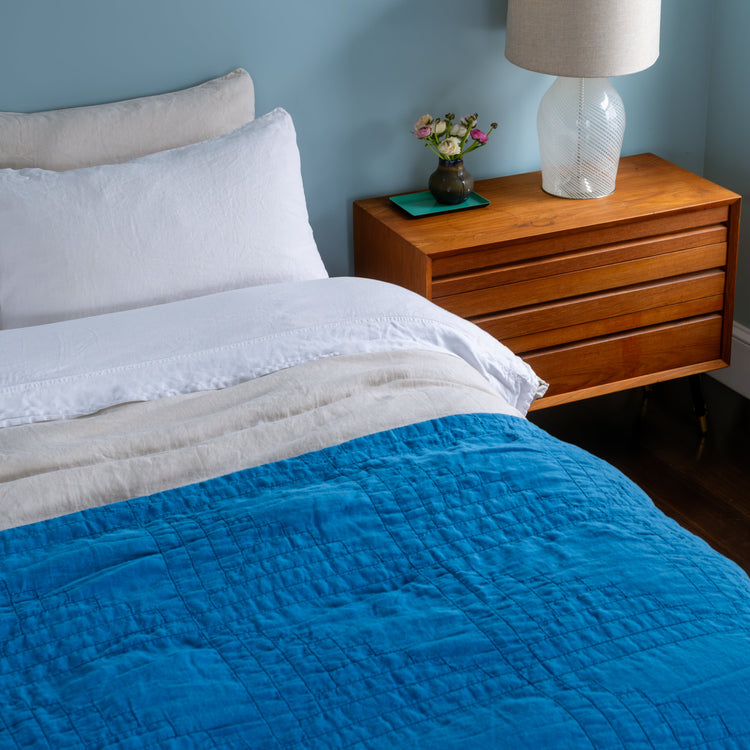 Bedroom with blue quilt, wooden nightstand, lamp, and decorative items.