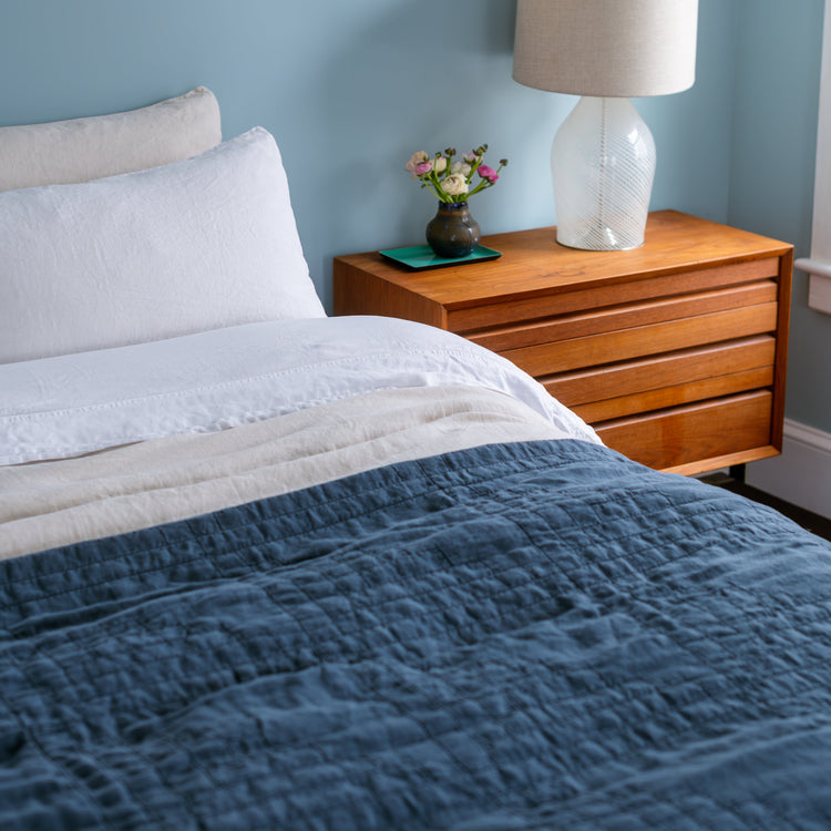 Bedroom with blue walls, a bed with a blue comforter, and a wooden nightstand with a lamp.