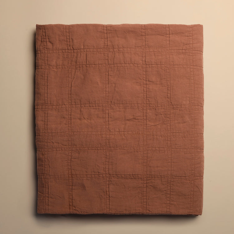brick red quilted blanket on a beige background