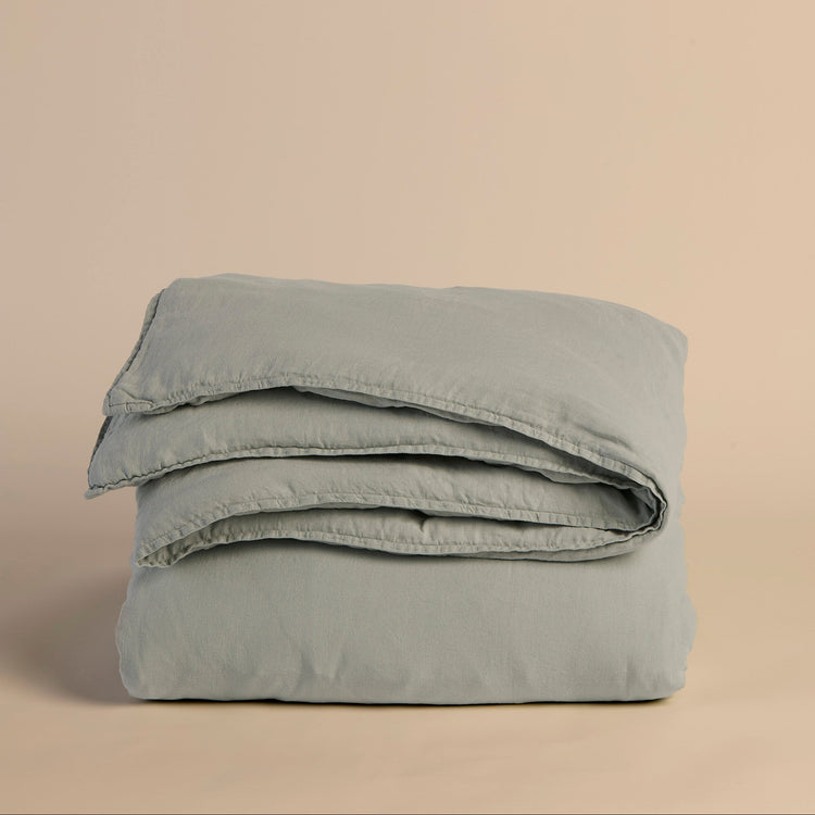 Folded light blue duvet cover and comforter on a beige background