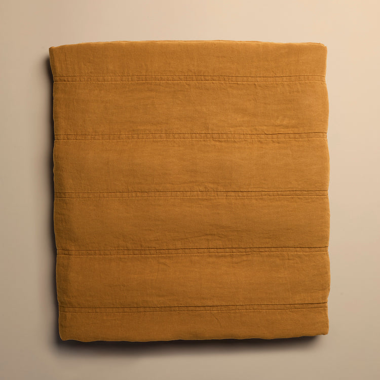 Folded mustard yellow quilt on a beige background