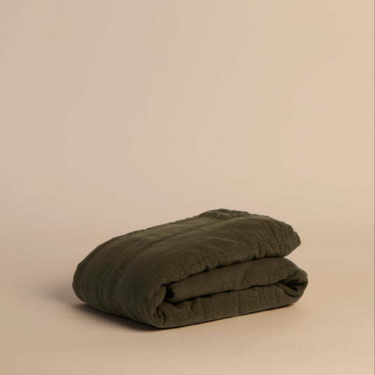 Folded dark green quilt on a beige background