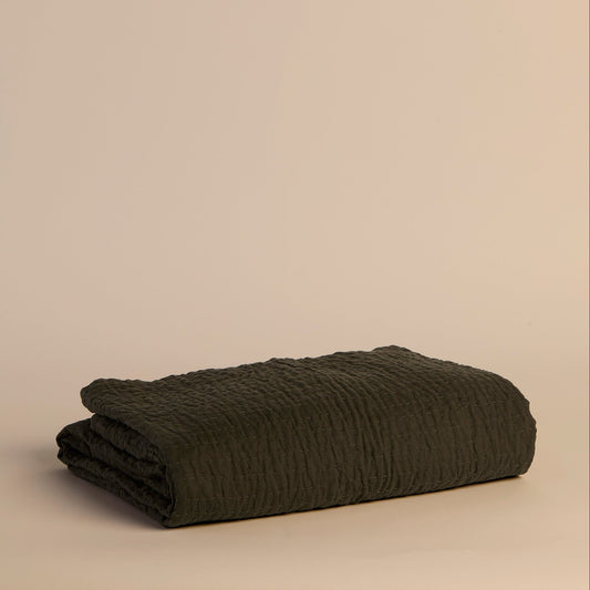Folded reversible dark green textured blanket on a beige background