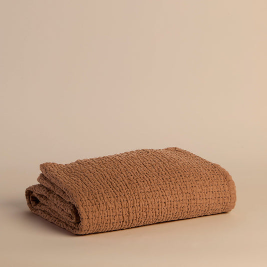 Folded copper textured blanket on a beige background