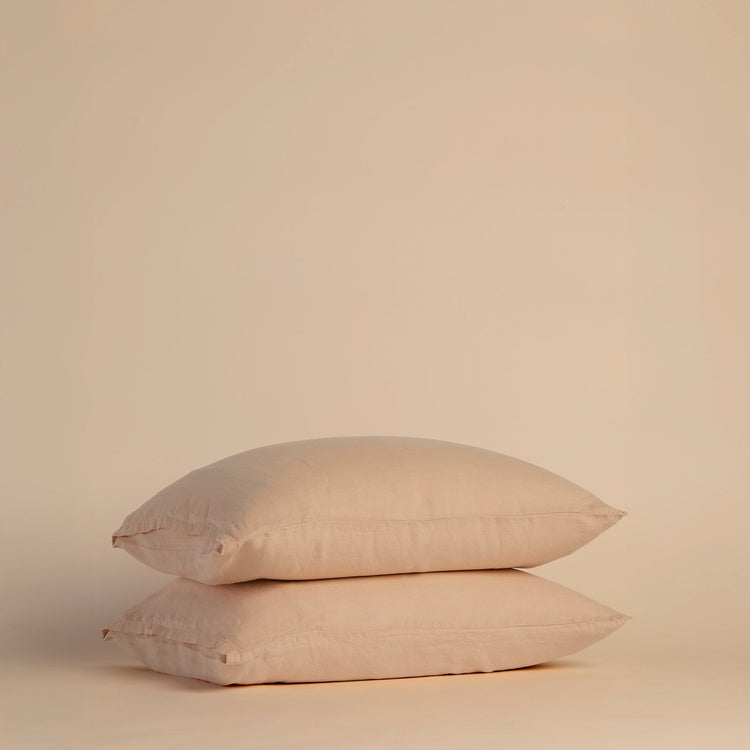 Two peach pillows with pillowcases stacked on a beige background