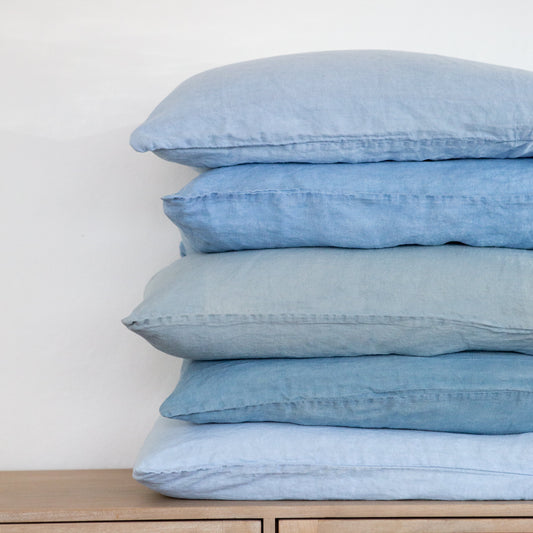 Stack of light blue indigo pillows on a wooden cabinet with a white background