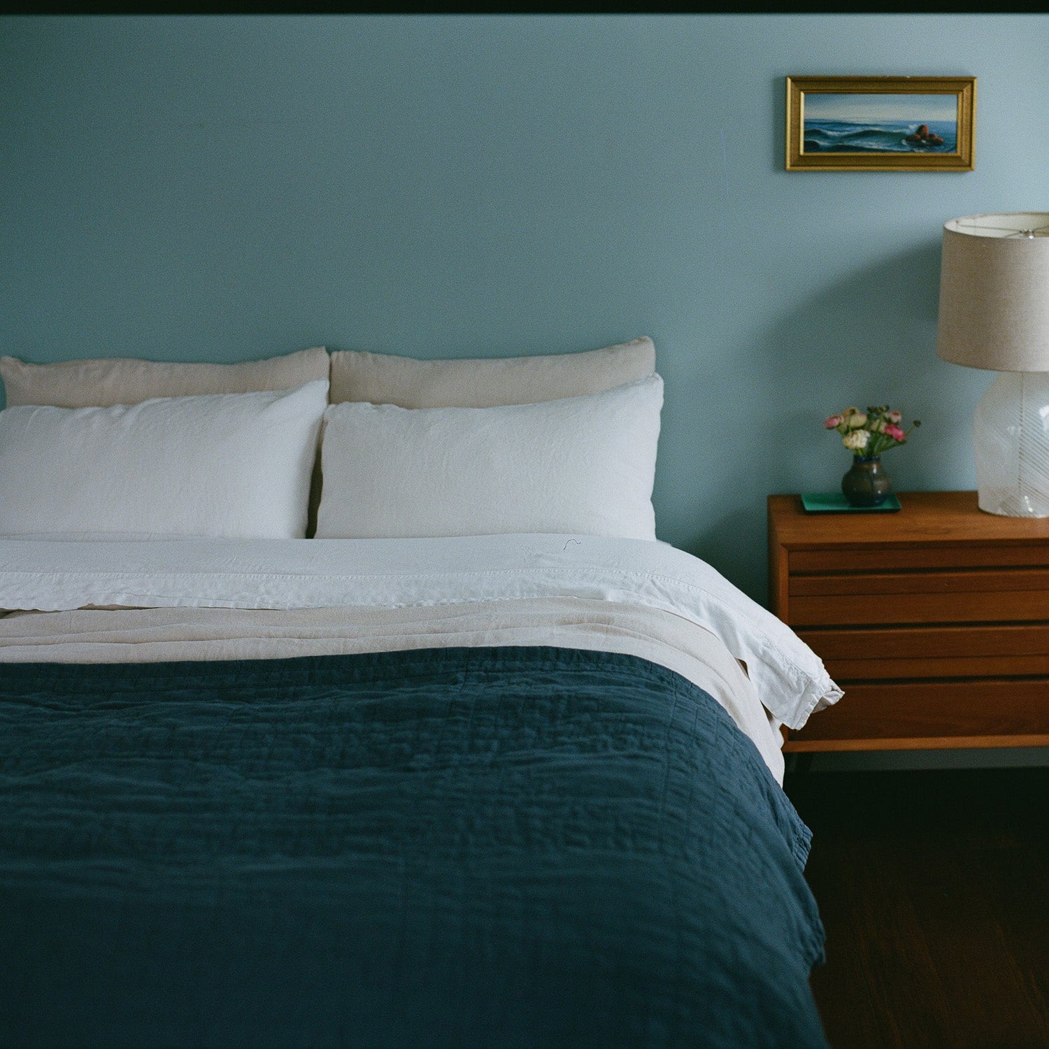 Bedroom with a bed, navy quilt, nightstand, and lamp against a light blue wall.