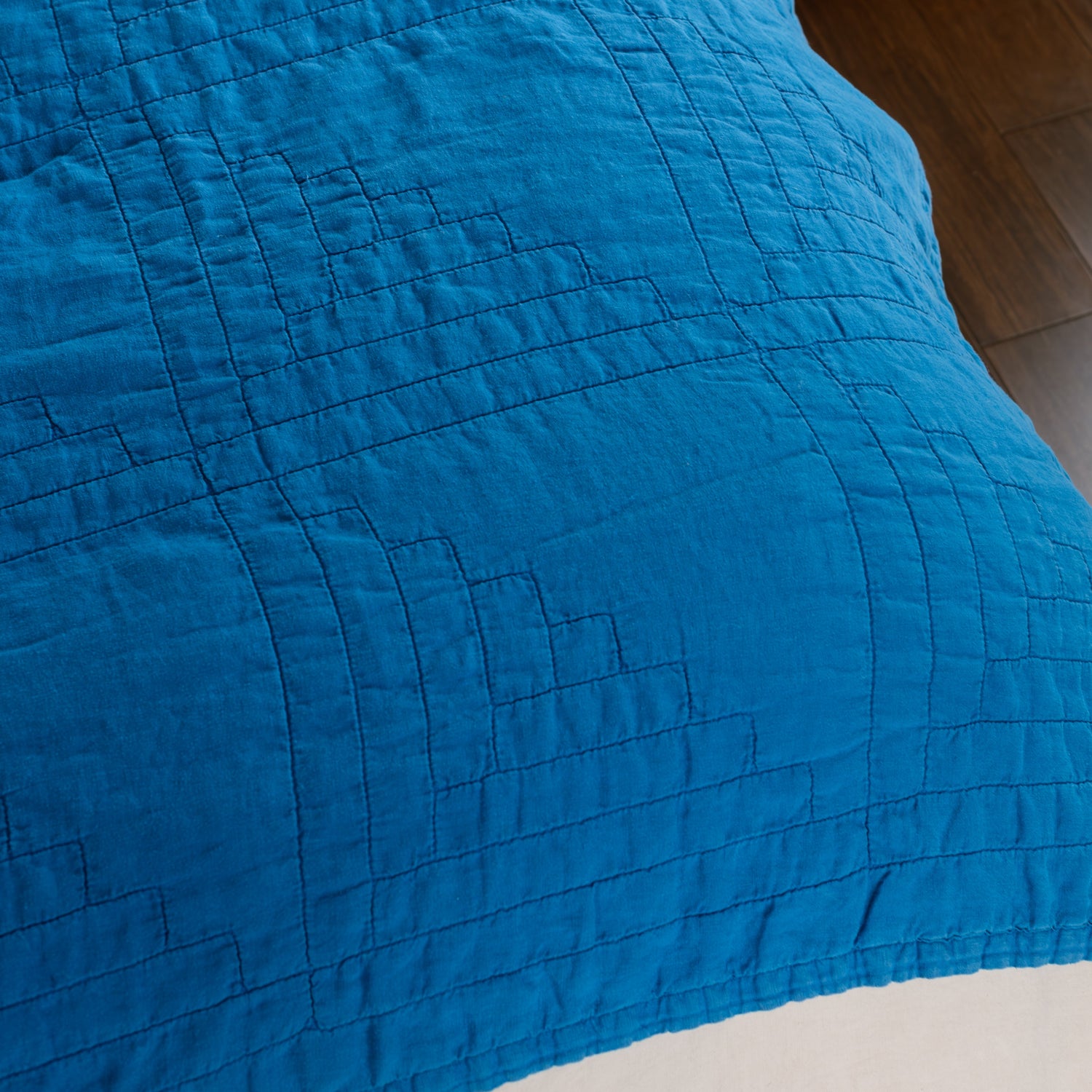 Close-up of a blue quilted coverlet on corner of bed
