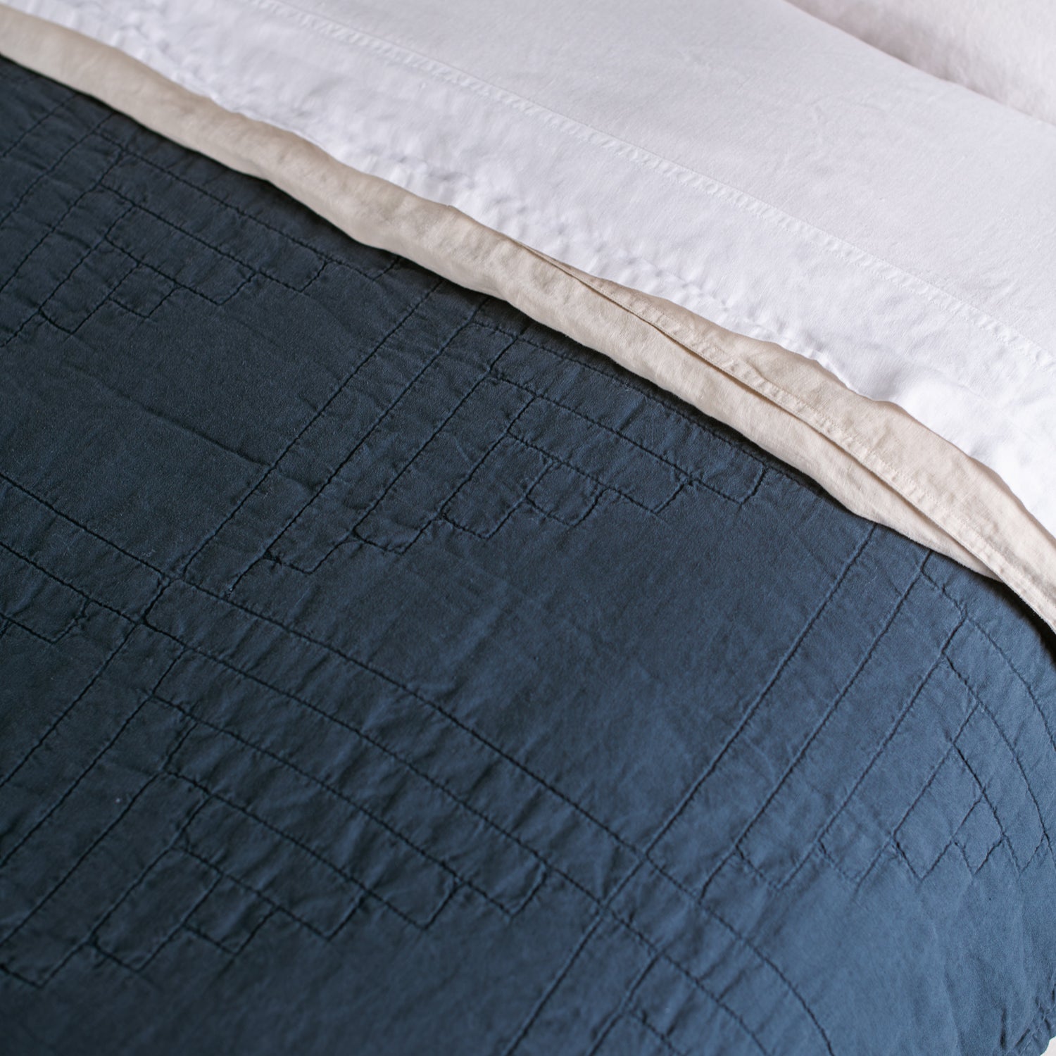 Blue quilted coverlet on a bed with white bedding