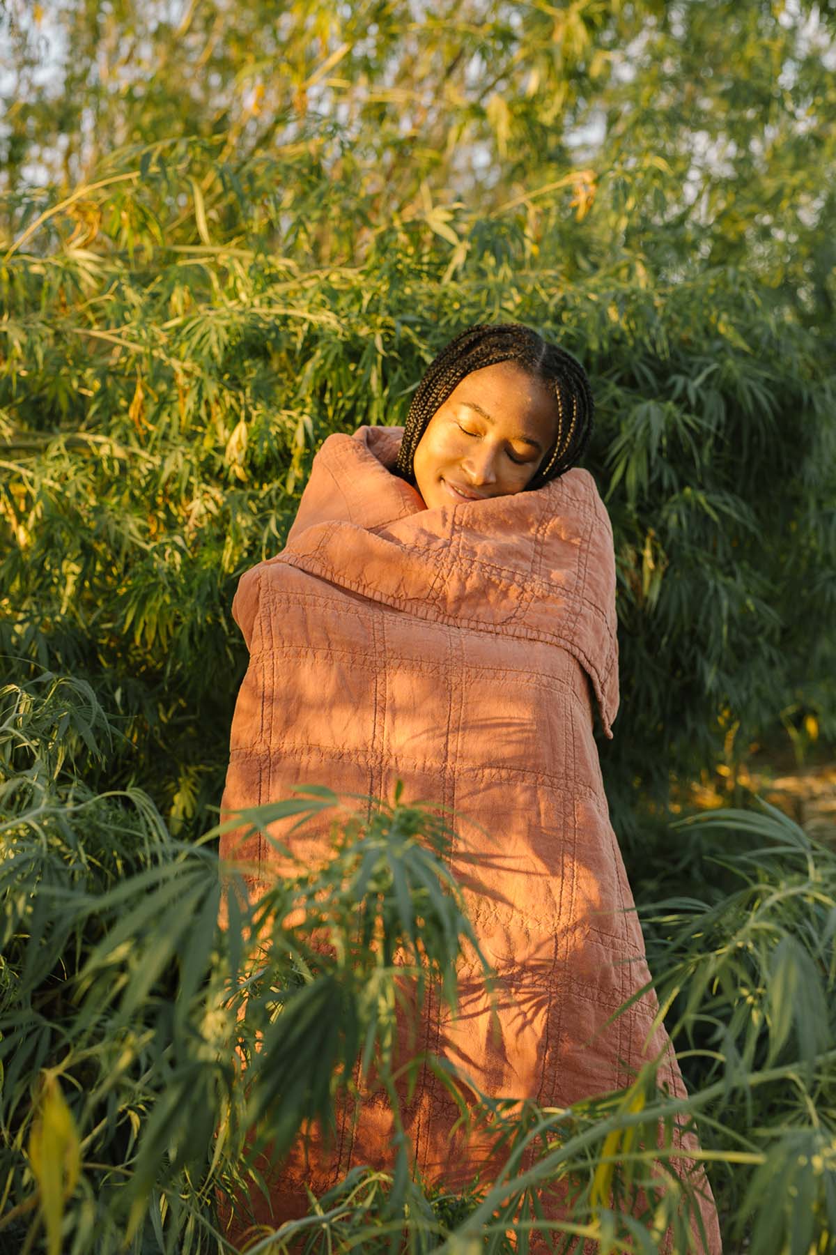 Woman wrapped in Hemp Daybreak Quilt, standing in hemp field