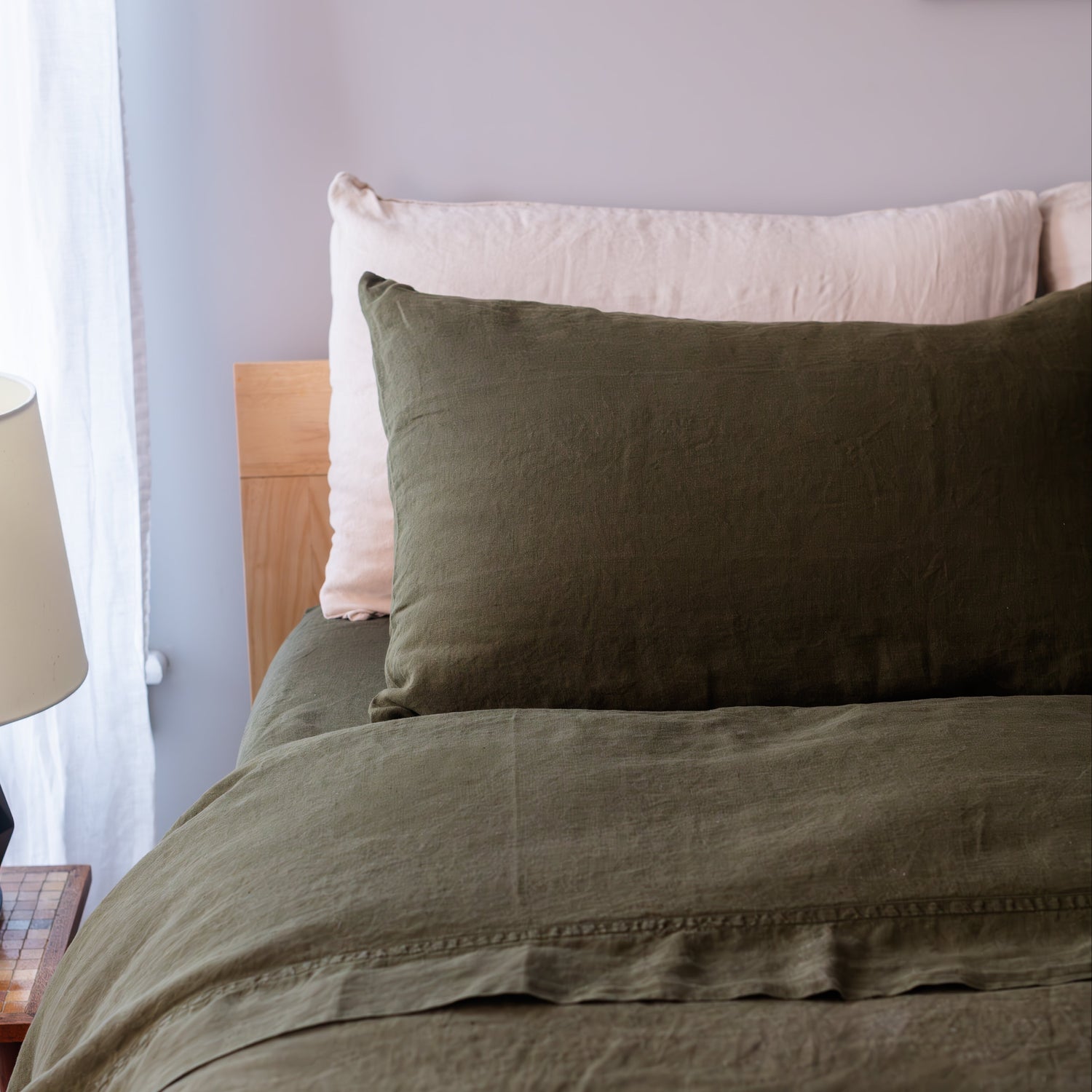 Bed with green bedding and natural pillows against a light gray wall.