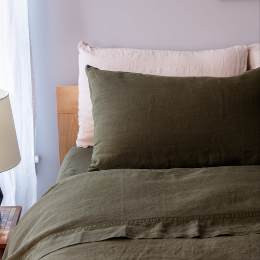 Bed with green bedding and natural pillows against a light gray wall.
