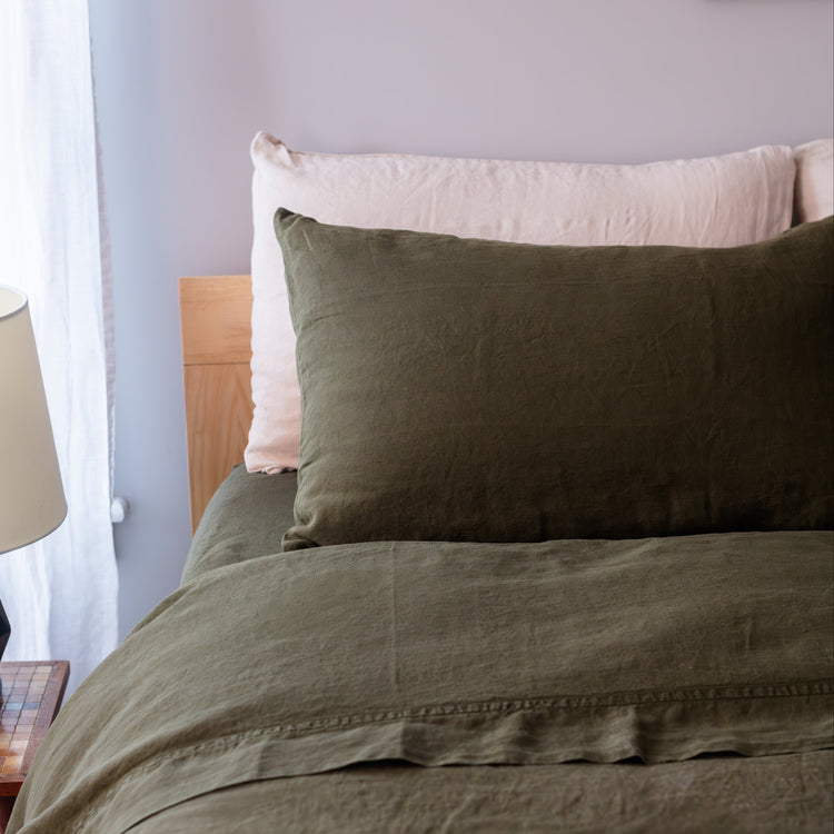 Bed with green bedding and natural pillows against a light gray wall.