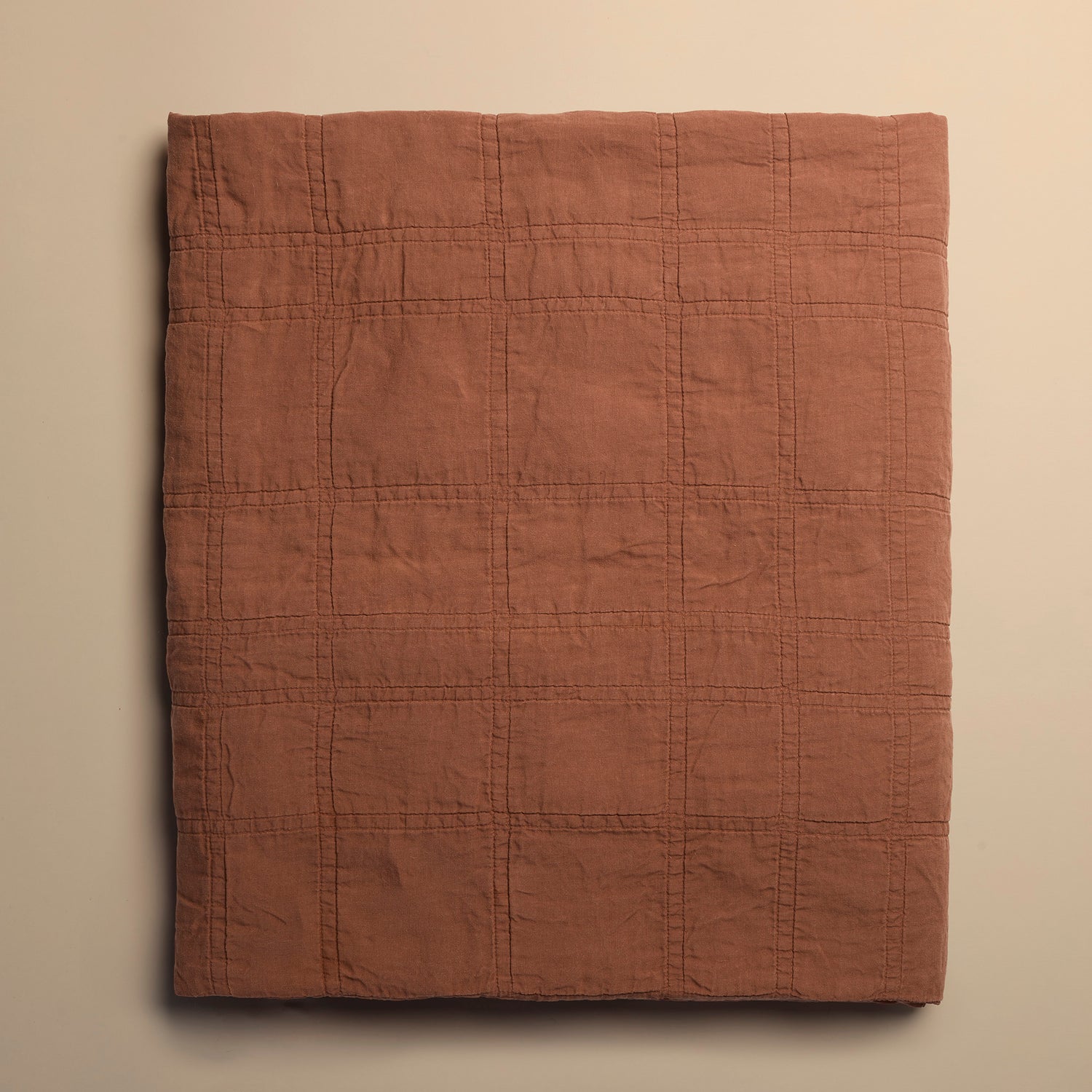 brick red quilted blanket on a beige background