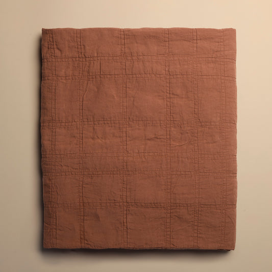 brick red quilted blanket on a beige background