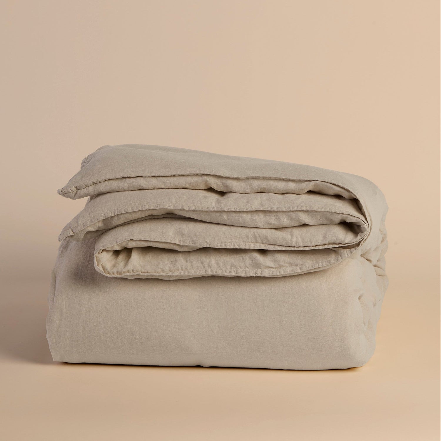 Folded light beige duvet cover and comforter on a beige background