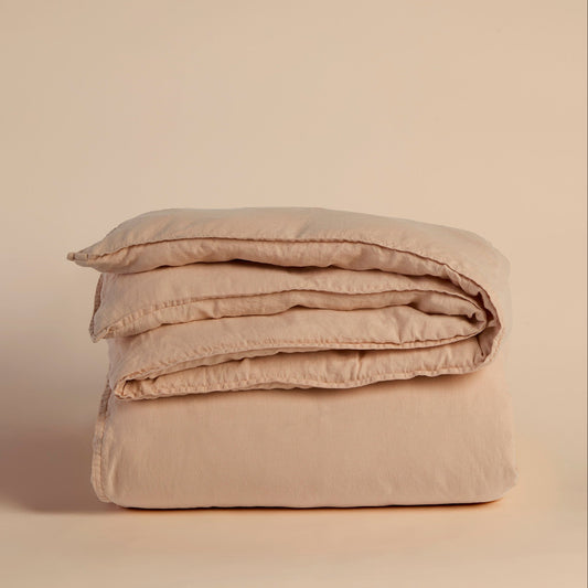 Folded peach duvet cover and comforter on a beige background