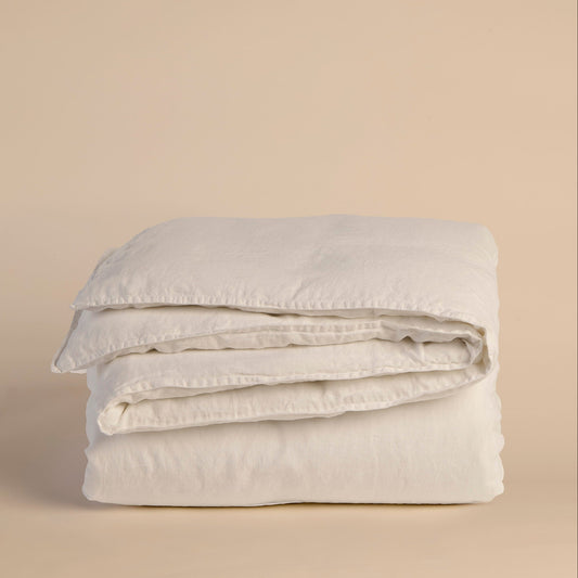 Folded white duvet cover and comforter on a beige background