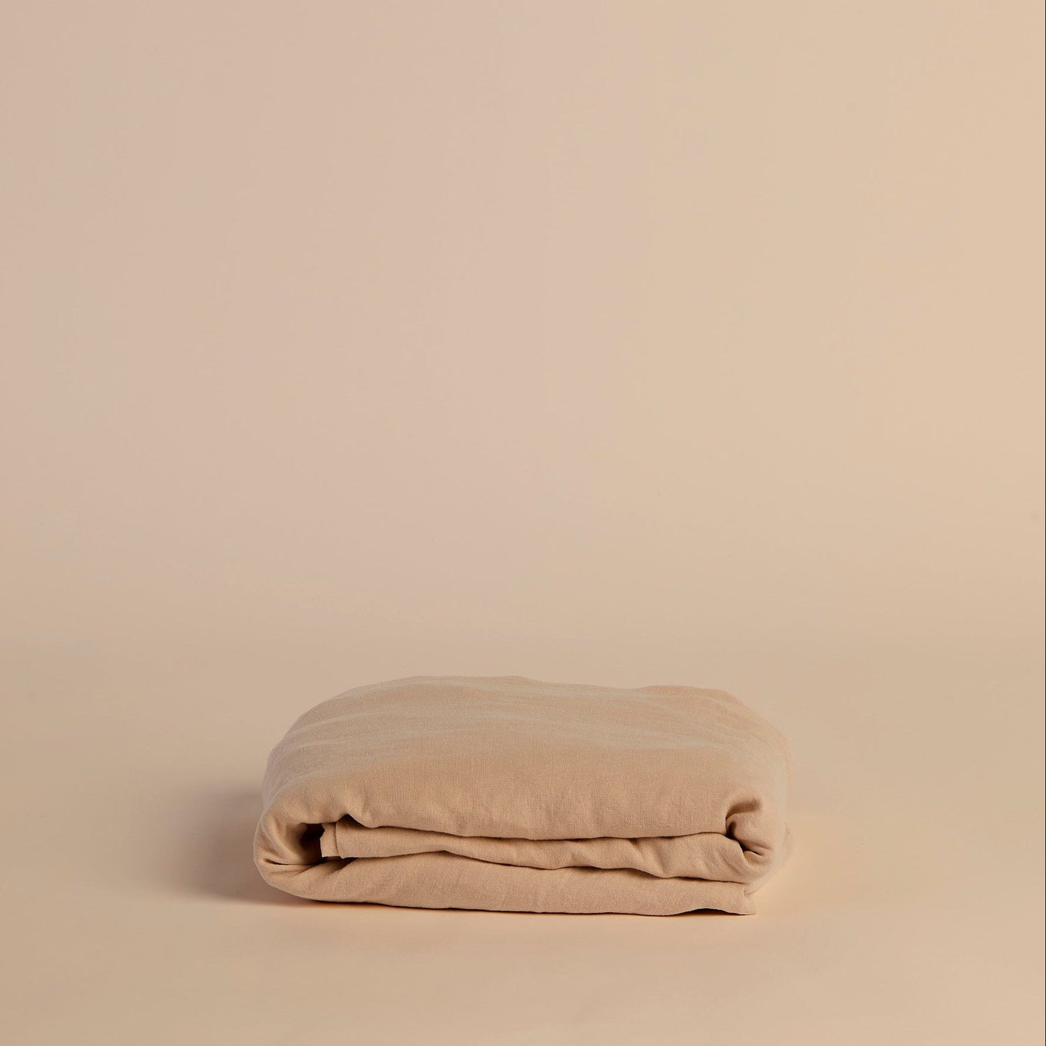 Folded peach fitted sheet on a beige background