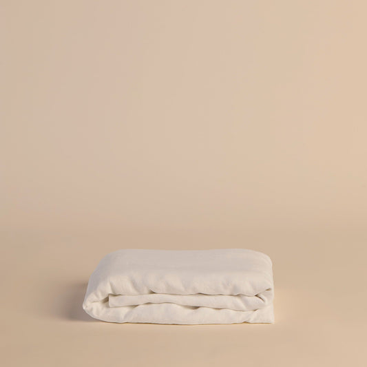 Folded white fitted sheet on a beige background