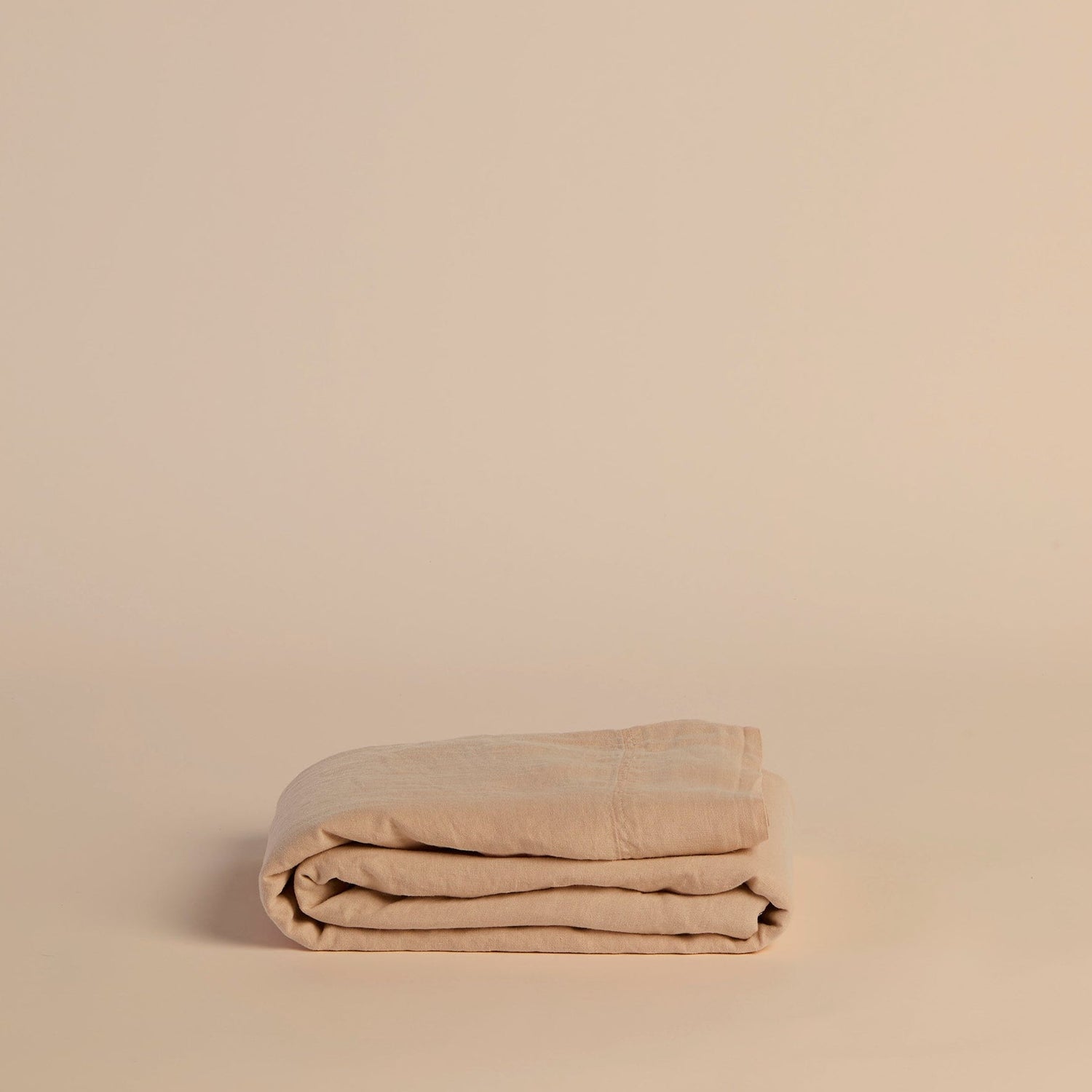 Folded peach flat sheet on a beige background