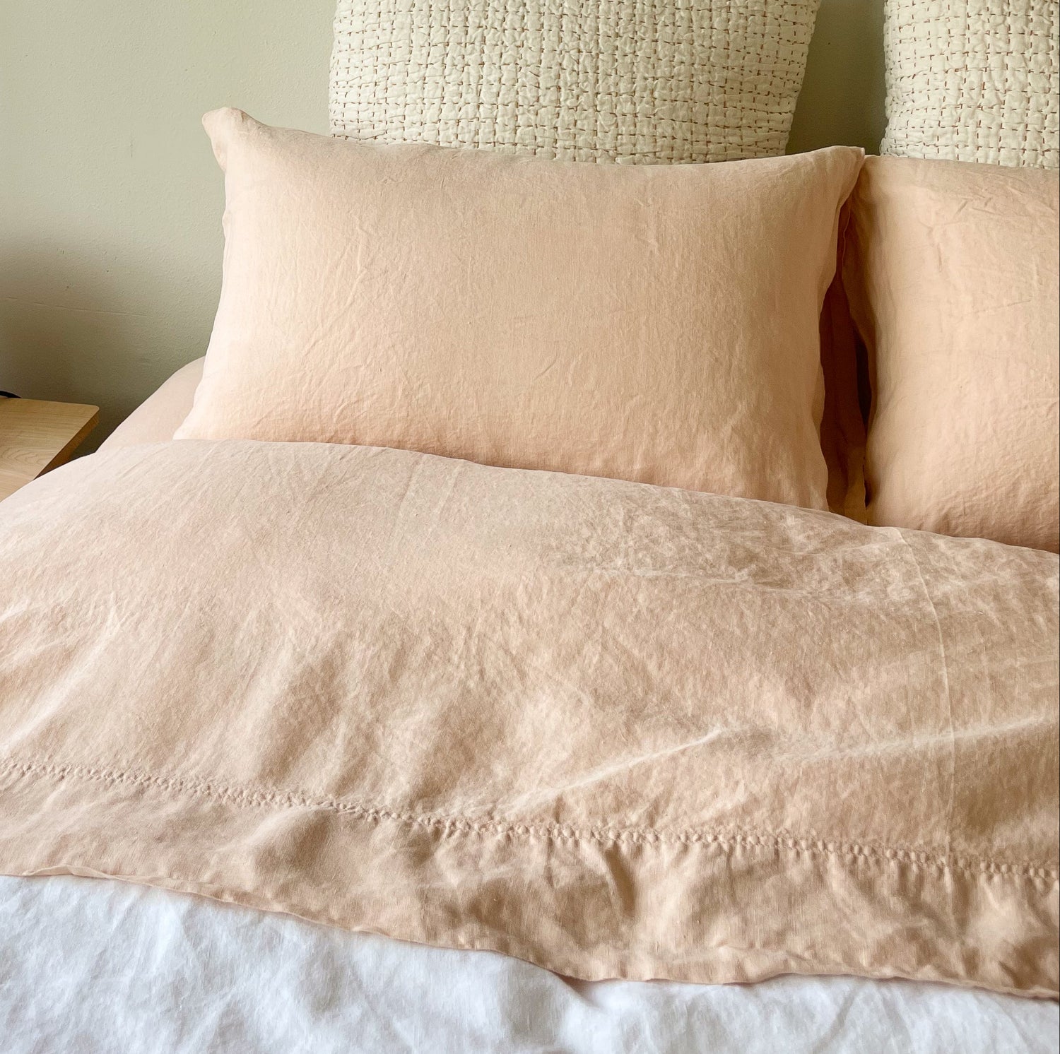 A photo of a bed with hemp sheets in a cozy room setting, featuring two pillows and a bedside lamp.