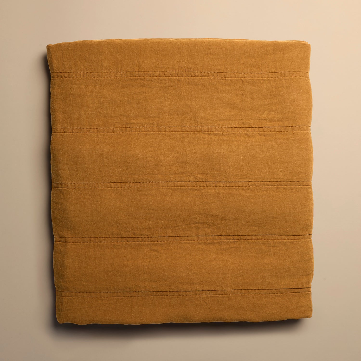 Folded mustard yellow quilt on a beige background