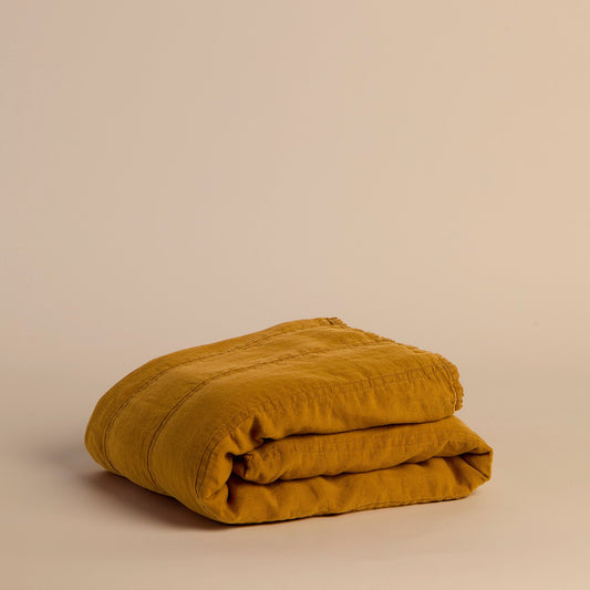Folded mustard yellow quilt on a beige background