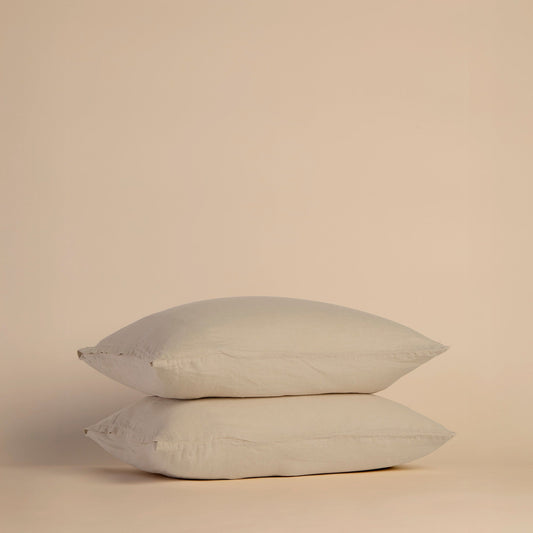 Two beige pillows with pillowcases stacked on a beige background