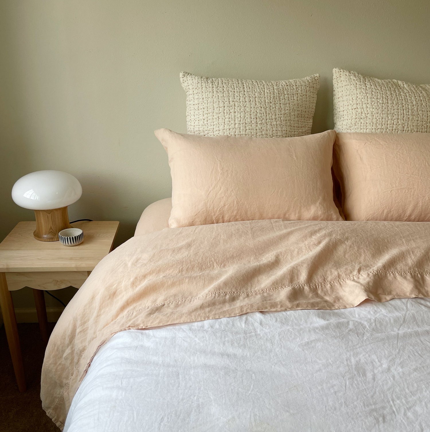 A hemp sheet set on a bed, including a top sheet, fitted sheet, and two pillowcases, with a lamp and a wooden nightstand beside the bed.
