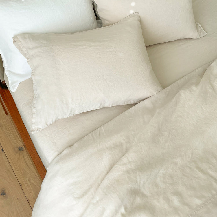 Beige textured duvet, sheets and pillows on a bed with wooden headboard.