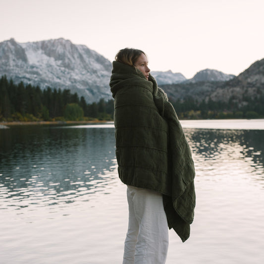 Person wrapped in a green quilt standing with mountains in the background