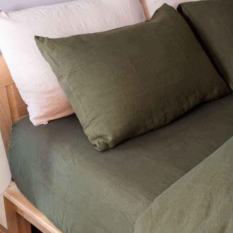 Dark green fitted sheet, duvet cover and pillows on a bed with a wooden headboard.