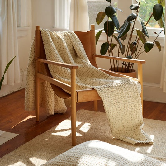Ivory hand-stitched quilt draped on leather chair in sunny room, with matching pillow on the floor.