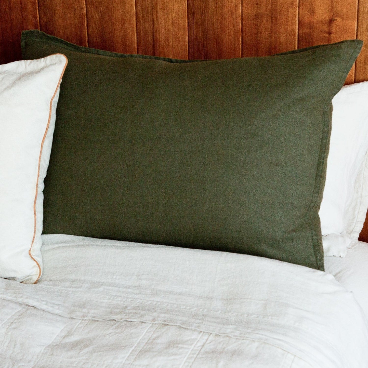 A green hemp sham displayed on a bed with a white duvet cover and a white pillow, against a wooden headboard.
