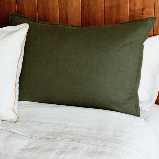 A green hemp sham displayed on a bed with a white duvet cover and a white pillow, against a wooden headboard.