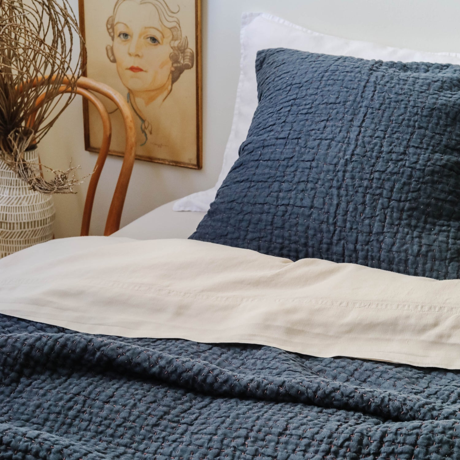 Hand stitched navy quilt on a bed with matching euro shams, portrait on wall