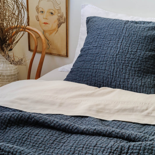 Hand stitched navy quilt on a bed with matching euro shams, portrait on wall